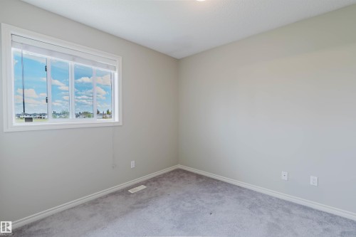 Interior room featuring a large window with white trim, light gray walls, white baseboards, and gray carpet flooring - 3534 Mclean Crescent, Edmonton, AB - Indoor Photo Showing Other Room