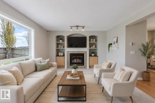 Spacious living area featuring a stone-surround fireplace with a wood mantel, built-in shelving, integrated cabinetry, and a large window overlooking the backyard - 3534 Mclean Crescent, Edmonton, AB - Indoor Photo Showing Living Room With Fireplace