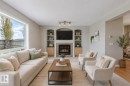 Spacious living area featuring a stone-surround fireplace with a wood mantel, built-in shelving, integrated cabinetry, and a large window overlooking the backyard - 3534 Mclean Crescent, Edmonton, AB  - Indoor Photo Showing Living Room With Fireplace 