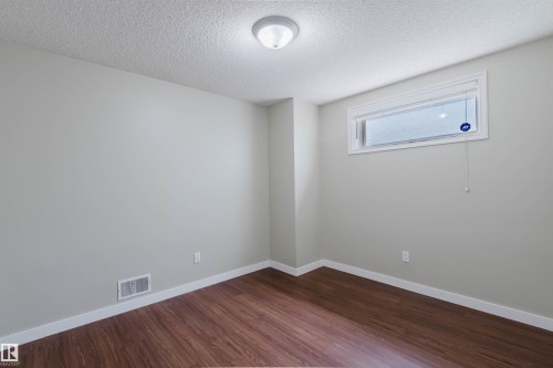 Light-filled room featuring wood-finish flooring, neutral wall paint, white baseboards, and a high-set window with blinds - 3534 Mclean Crescent, Edmonton, AB - Indoor Photo Showing Other Room