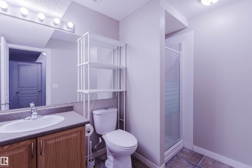 Full bathroom featuring a single vanity with wood-finish cabinetry, a built-in shower with a glass enclosure, a white toilet, and tile flooring - 3534 Mclean Crescent, Edmonton, AB - Indoor Photo Showing Bathroom