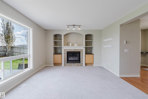 Living area featuring a gas fireplace with stone surround and mantle, built-in arched shelving, built-in wood cabinetry, and track lighting - 3534 Mclean Crescent, Edmonton, AB - Indoor Photo Showing Other Room With Fireplace