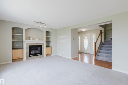 Living area featuring a gas fireplace with stone tile surround, built-in shelving, track lighting, and soft grey carpeting - 3534 Mclean Crescent, Edmonton, AB - Indoor Photo Showing Living Room With Fireplace