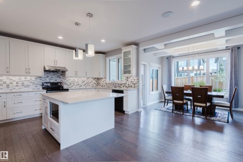Open-concept kitchen featuring an oversized island with an integrated microwave, white shaker cabinetry, a tile backsplash, and dark wood-finish flooring - 3571 Keswick Boulevard, Edmonton, AB - Indoor Photo Showing Kitchen With Upgraded Kitchen