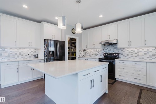 Spacious kitchen featuring an expansive central island with a light-toned countertop, white cabinetry with silver-tone hardware, and wood-finish flooring - 3571 Keswick Boulevard, Edmonton, AB - Indoor Photo Showing Kitchen With Upgraded Kitchen