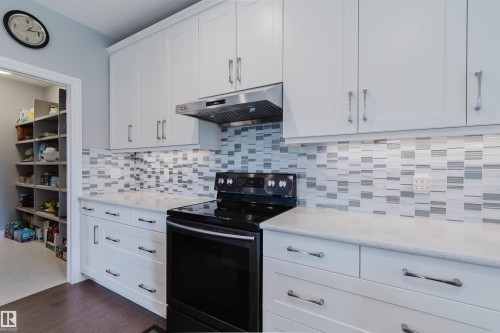 White shaker-style cabinetry with chrome hardware, a patterned tile backsplash, and a built-in stainless steel range hood - 3571 Keswick Boulevard, Edmonton, AB - Indoor Photo Showing Kitchen