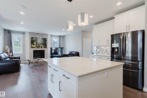 Open-concept living area featuring a kitchen island with stone countertop, white shaker cabinetry, and wood-finish flooring - 3571 Keswick Boulevard, Edmonton, AB - Indoor