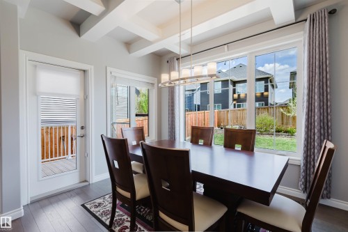 Dining area featuring coffered ceilings, contemporary linear chandelier, wood-finish flooring, and ample natural light from large windows - 3571 Keswick Boulevard, Edmonton, AB - Indoor Photo Showing Other Room