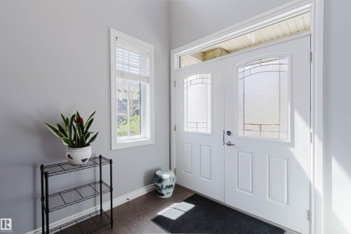 Double entry doors featuring decorative glass inserts and a transom window, complemented by wood-finish flooring and a single-pane window with white blinds - 3571 Keswick Boulevard, Edmonton, AB - Indoor Photo Showing Other Room