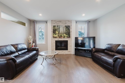 Living space featuring wood-finish flooring, a stacked stone fireplace surround, and recessed lighting - 3571 Keswick Boulevard, Edmonton, AB - Indoor Photo Showing Living Room With Fireplace