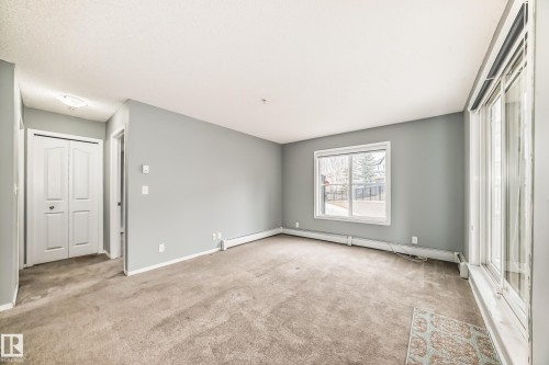 This spacious room features neutral gray walls and carpeting, with a large window and glass sliding door providing natural light - 101 530 Watt Boulevard, Edmonton, AB - Indoor Photo Showing Other Room