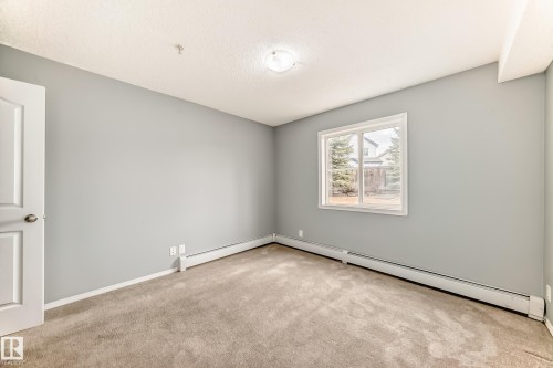 The property features a bright room with light grey walls, carpeted flooring, and a window providing views of the outdoors - 101 530 Watt Boulevard, Edmonton, AB - Indoor Photo Showing Other Room