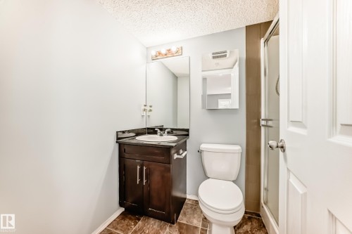 Bathroom featuring a dark wood vanity with a white basin and granite countertop, a toilet, and a glass-enclosed shower - 101 530 Watt Boulevard, Edmonton, AB - Indoor Photo Showing Bathroom