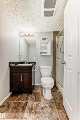 The bathroom features a vanity with a dark wood cabinet, a white toilet, and a stand-up shower with a glass enclosure - 101 530 Watt Boulevard, Edmonton, AB - Indoor Photo Showing Bathroom