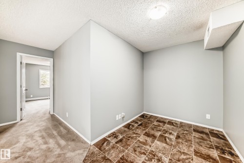 This space features neutral-toned walls, a textured ceiling, and a combination of carpeted and tiled flooring - 101 530 Watt Boulevard, Edmonton, AB - Indoor Photo Showing Other Room