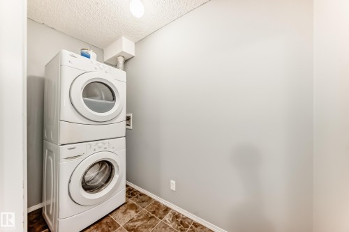 Dedicated laundry area featuring a white stackable washer and dryer, tiled flooring, and light gray walls - 101 530 Watt Boulevard, Edmonton, AB - Indoor Photo Showing Laundry Room