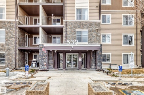 The property features a building with a stone and siding exterior, balconies with dark railings, and a welcoming main entrance with glass doors - 101 530 Watt Boulevard, Edmonton, AB - Outdoor With Facade