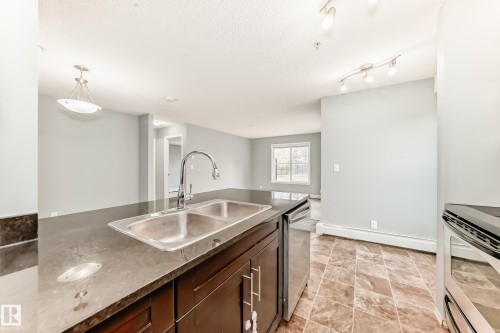 Kitchen featuring a double stainless steel sink, dark cabinetry, and a dark countertop - 101 530 Watt Boulevard, Edmonton, AB - Indoor Photo Showing Kitchen With Double Sink