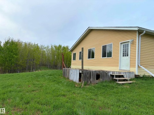 Exterior featuring yellow siding, multiple windows, a white entry door, and a partially covered deck with stairs - 60016 Rr 41, Rural Barrhead County, AB - Outdoor