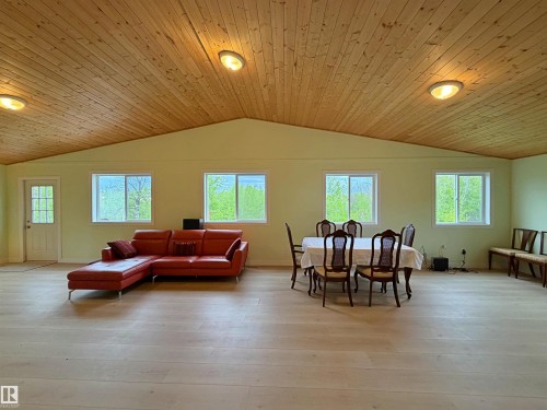 Spacious room featuring a vaulted wood-plank ceiling, light wood-finish flooring, multiple windows, and a paneled entry door - 60016 Rr 41, Rural Barrhead County, AB - Outdoor