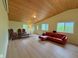 Spacious room featuring a vaulted wood-plank ceiling, light wood-finish flooring, multiple windows, a wall-mounted air conditioning unit, and a glass-paneled door - 