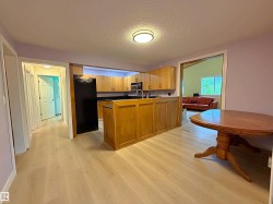 Open-concept kitchen featuring wood-finish cabinetry, a central island, black appliances, and light wood-finish flooring - 