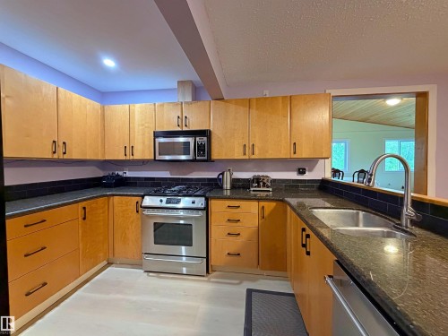 Kitchen featuring extensive wood cabinetry, dark speckled countertops, and a subway tile backsplash - 60016 Rr 41, Rural Barrhead County, AB - Indoor Photo Showing Kitchen