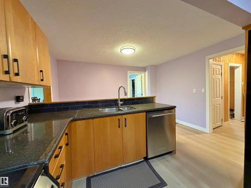 Kitchen featuring wood-finish cabinetry, dark speckled countertops, a stainless steel dishwasher, and a stainless steel sink with a gooseneck faucet - 60016 Rr 41, Rural Barrhead County, AB - Indoor Photo Showing Kitchen