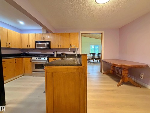 Kitchen featuring light wood-finish cabinetry, dark countertops, and stainless steel appliances including a range and microwave - 60016 Rr 41, Rural Barrhead County, AB - Indoor Photo Showing Kitchen With Double Sink