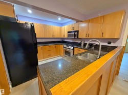 Kitchen featuring light wood cabinetry, dark granite countertops, stainless steel appliances including a built-in microwave and gas range, and an undermount sink with a gooseneck faucet - 