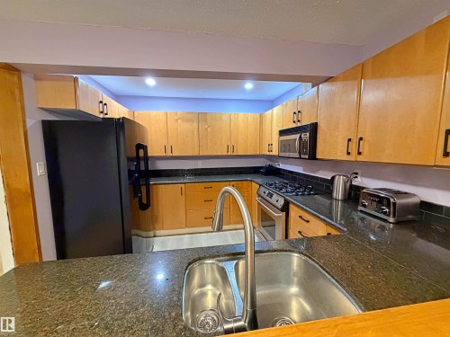 Kitchen featuring dark granite countertops, stainless steel sink with high-arc faucet, light wood cabinetry, and a black tile backsplash - 60016 Rr 41, Rural Barrhead County, AB - Indoor Photo Showing Kitchen With Double Sink
