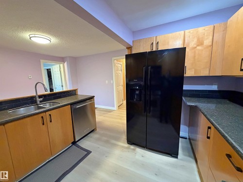 Kitchen featuring light wood-finish cabinetry, dark granite countertops, a stainless-steel dishwasher, and light wood-finish flooring - 60016 Rr 41, Rural Barrhead County, AB - Indoor Photo Showing Kitchen With Double Sink