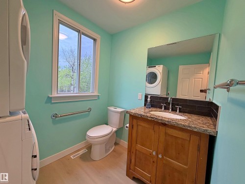 Stacked laundry appliances alongside a windowed bath featuring a wood vanity with a stone countertop, an undermount sink, and a dark subway tile backsplash - 60016 Rr 41, Rural Barrhead County, AB - Indoor Photo Showing Bedroom