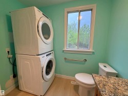 Dedicated laundry area featuring stacked appliances, a window, and a toilet - 