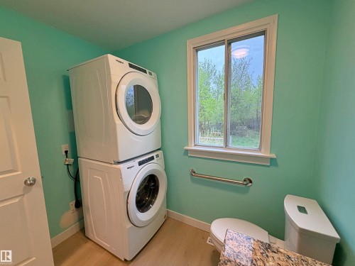 Laundry area featuring a stackable washer and dryer, light wood-finish flooring, a white-framed window, and a white door with a round silver knob - 60016 Rr 41, Rural Barrhead County, AB - Indoor Photo Showing Bathroom