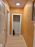 Hallway featuring wood paneling walls, light wood-finish flooring, white trim, recessed ceiling lighting, and white paneled doors - 