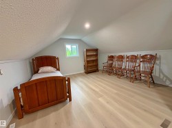 Spacious attic room featuring light-toned wood-finish flooring, a vaulted ceiling, recessed lighting, and a window for natural illumination - 