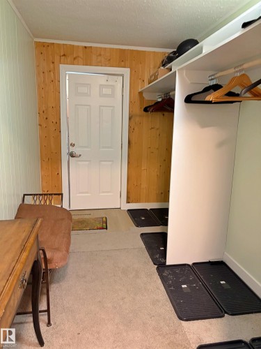 Entryway featuring a paneled door, wood-finish accent wall, built-in shelving, clothing rod, and carpeting - 60016 Rr 41, Rural Barrhead County, AB - Indoor