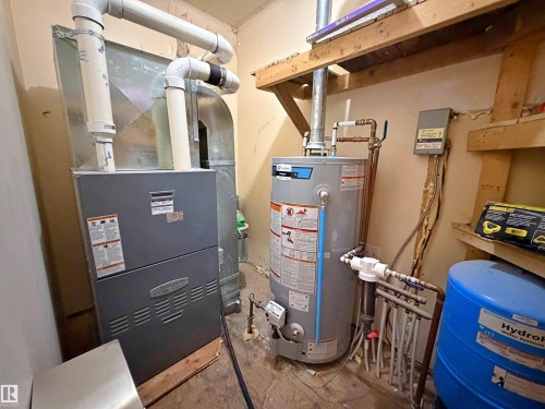 Utility room featuring a furnace, water heater, water treatment system, and exposed wood shelving - 60016 Rr 41, Rural Barrhead County, AB - Indoor