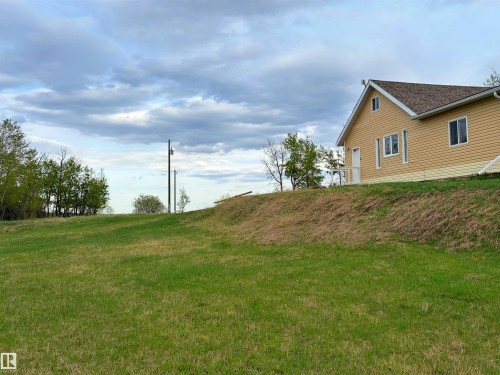 Expansive grassy terrain with a gentle slope leading to a residence featuring a light yellow siding exterior, white trim, and a brown shingle roof - 60016 Rr 41, Rural Barrhead County, AB - Outdoor