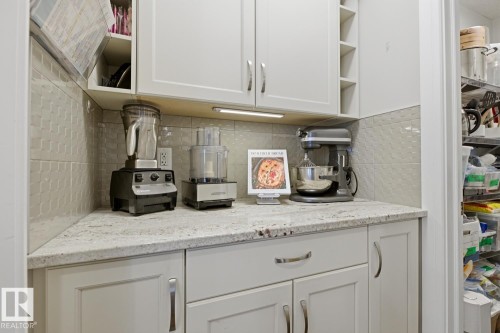 Kitchen nook featuring white cabinetry with silver hardware, speckled light-toned countertop, and a textured tile backsplash - 1359 Westerra Drive, Stony Plain, AB - Indoor Photo Showing Kitchen