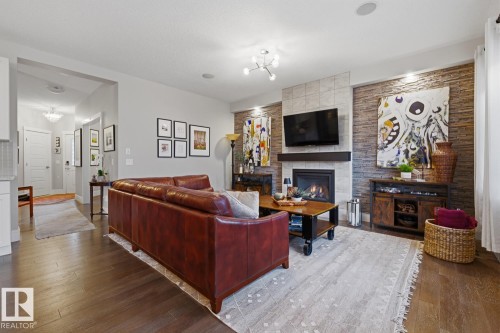 Living area featuring rich wood-finish flooring, a contemporary fireplace with a sleek mantel, and a multi-textured accent wall - 1359 Westerra Drive, Stony Plain, AB - Indoor Photo Showing Living Room With Fireplace