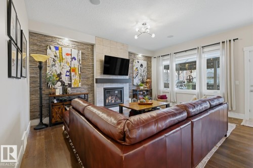 Living area featuring a floor-to-ceiling stacked stone accent wall, a gas fireplace with tile surround and dark mantel, wood-finish flooring, recessed lighting, and a multi-light ceiling fixture - 1359 Westerra Drive, Stony Plain, AB - Indoor Photo Showing Living Room With Fireplace