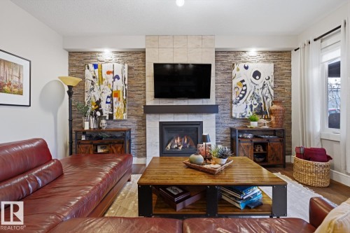 Living area featuring a gas fireplace with a tiled surround and wood mantel, flanked by stacked stone accent walls - 1359 Westerra Drive, Stony Plain, AB - Indoor Photo Showing Living Room With Fireplace