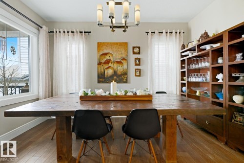 Dining space featuring wood-finish flooring, a large window with white trim, a multi-bulb chandelier, and built-in shelving with integrated cabinetry - 1359 Westerra Drive, Stony Plain, AB - Indoor Photo Showing Other Room
