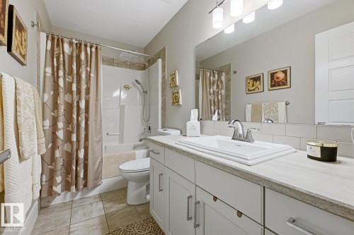 Bathroom featuring a white vanity with panel cabinetry and a light-toned countertop, a rectangular undermount sink with a chrome faucet, and a large mirror - 1359 Westerra Drive, Stony Plain, AB - Indoor Photo Showing Bathroom