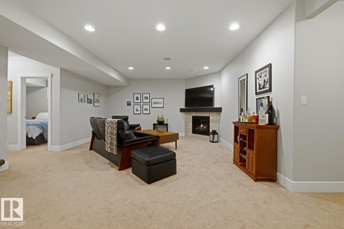 Spacious carpeted living area featuring a corner fireplace with stone surround, a dark wood mantel, and recessed lighting - 1359 Westerra Drive, Stony Plain, AB - Indoor