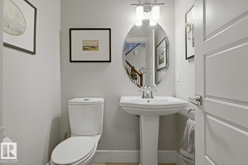 Pedestal sink with chrome faucet, oval mirror, and two-light vanity fixture - 1359 Westerra Drive, Stony Plain, AB - Indoor Photo Showing Bathroom