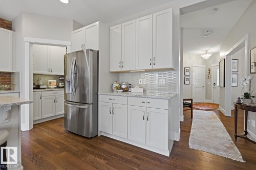 Kitchen featuring wood-finish flooring, white shaker cabinetry, light-toned granite countertops, and a full-height tile backsplash - 1359 Westerra Drive, Stony Plain, AB - Indoor Photo Showing Kitchen