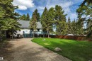 White siding exterior with a dark gray shingle roof, featuring a raised deck with blue railings and stairs, a concrete driveway, a manicured lawn, and mature evergreen trees - 305 3 St, Rural Wetaskiwin County, AB  - Outdoor 